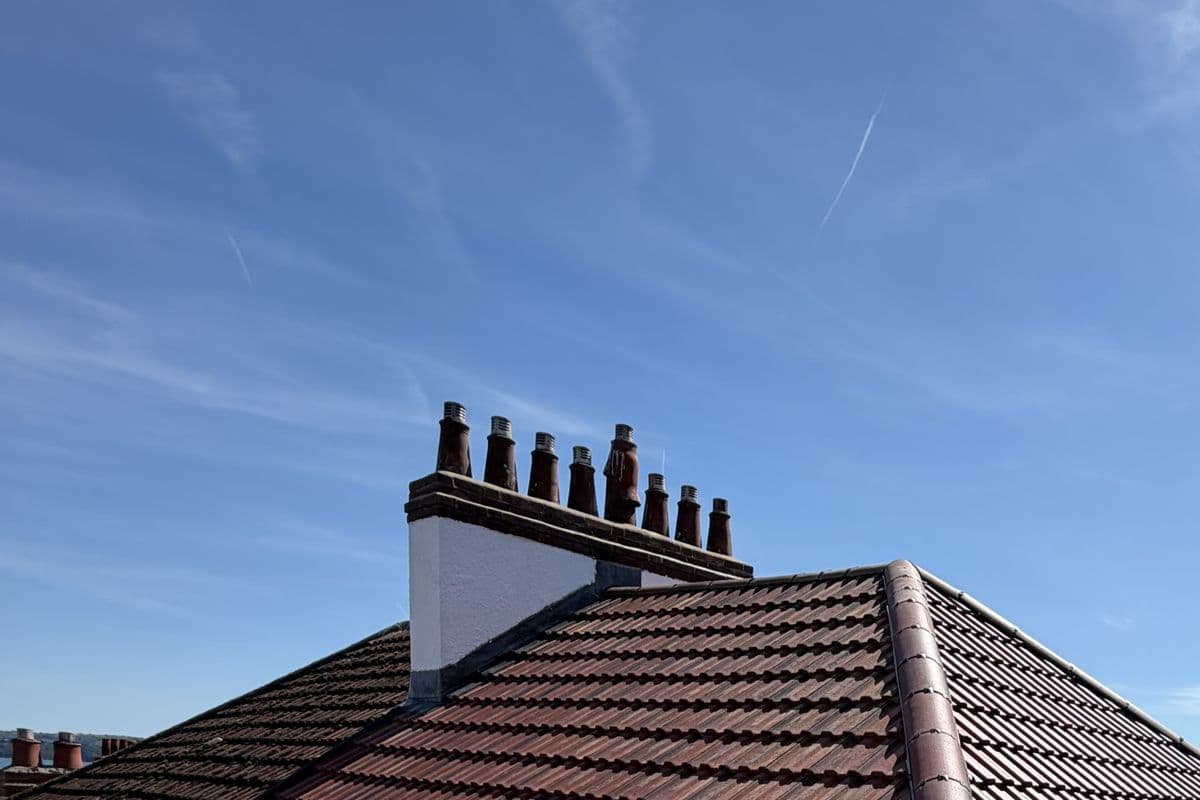 A repointed chimney stack with clay pots on a newly tiled roof